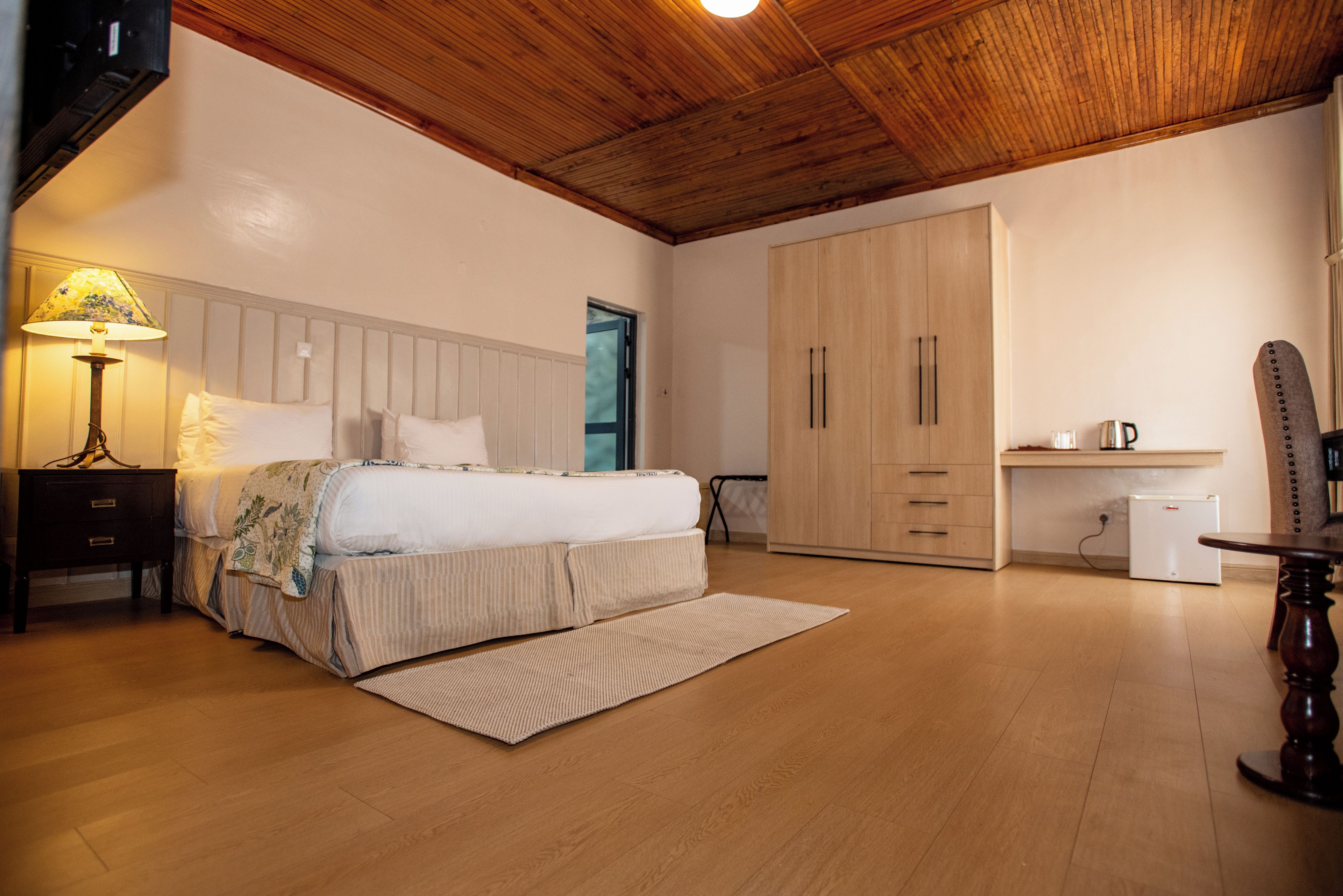 Un dormitorio con cama, mesita de noche, lámpara, armario y una pequeña zona de kitchenette.