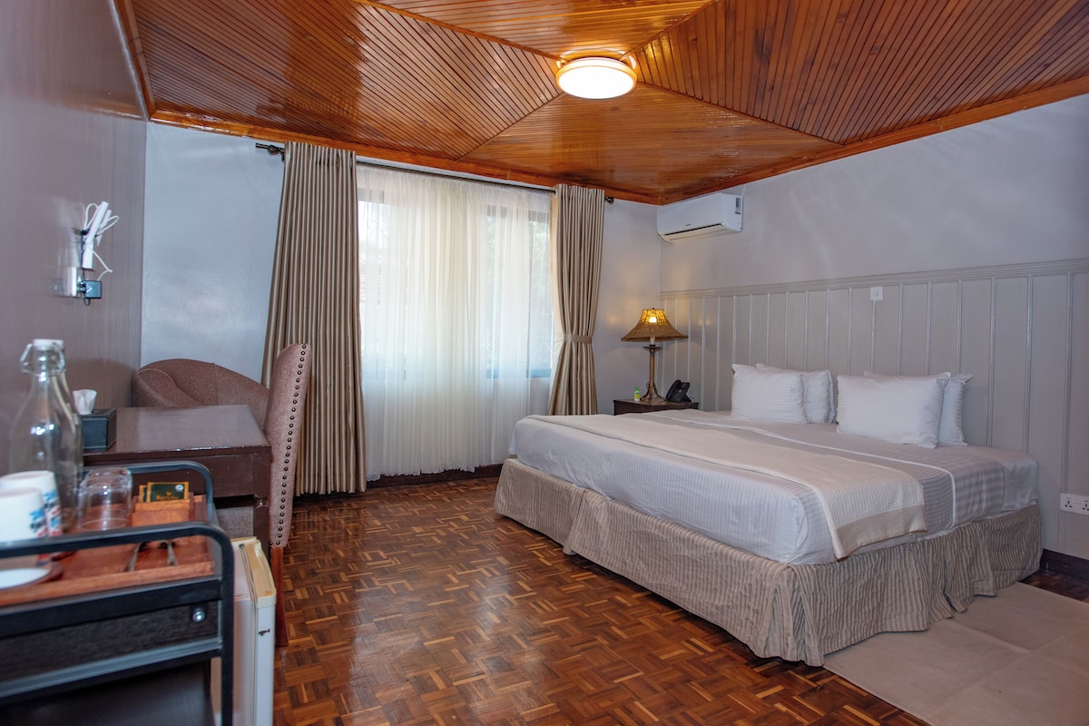 Une chambre d’hôtel avec un plafond en bois, un lit avec une literie blanche, une table de chevet avec une lampe, un plancher en bois et une fenêtre avec des rideaux.
