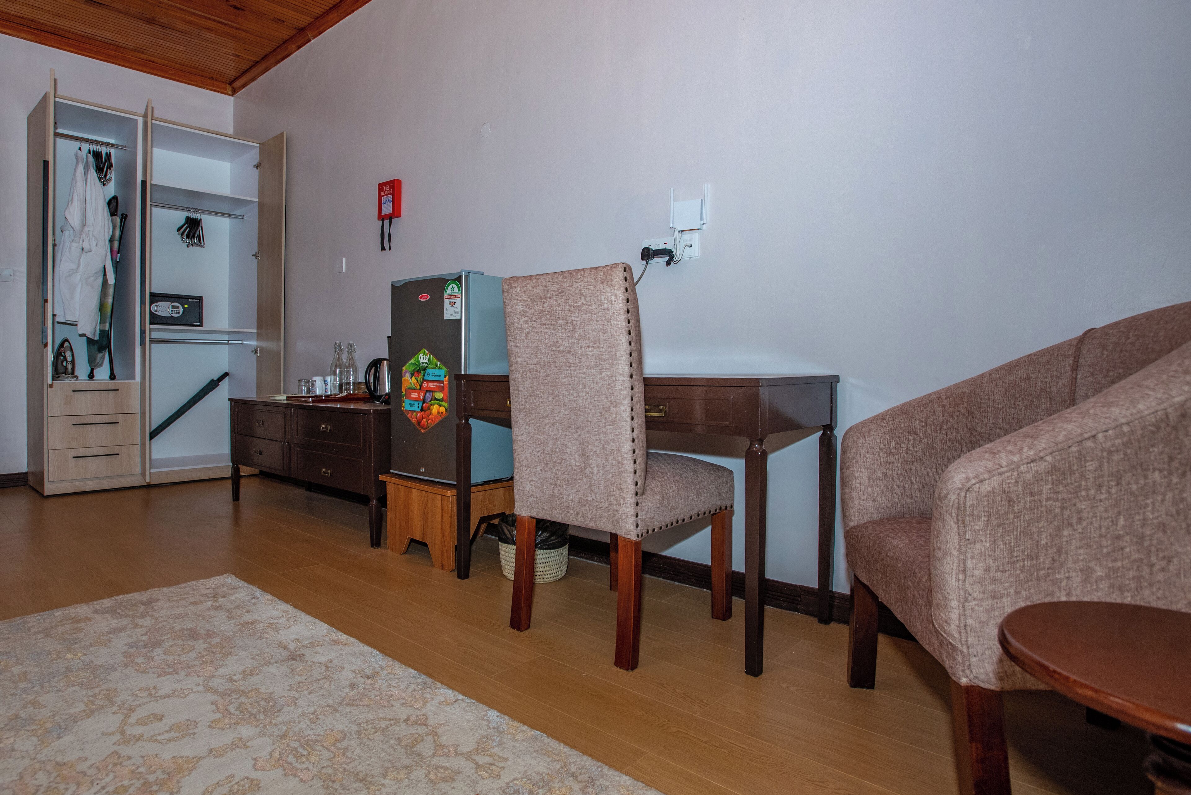 A living room with a wooden floor, a sofa, a dining table, and a kitchen area with a refrigerator and cabinets.