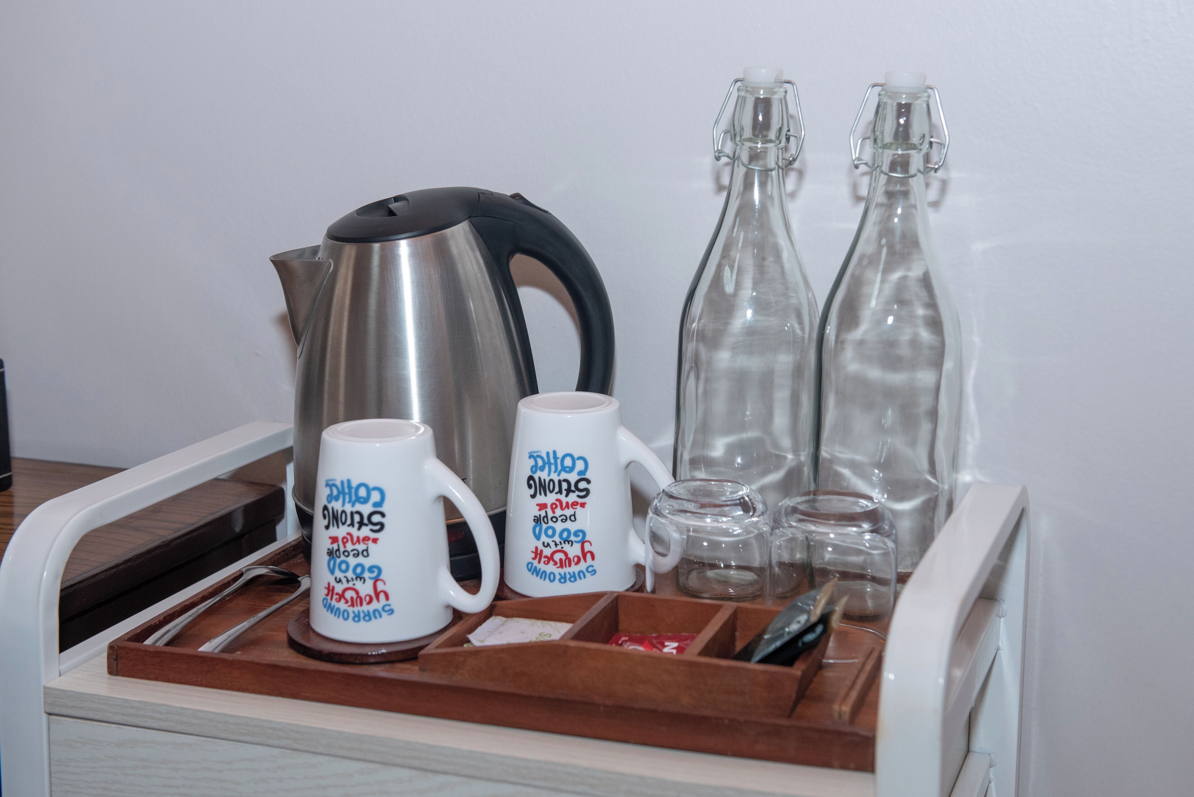 A tray with a stainless steel kettle, two white mugs with text, and two clear glass bottles.