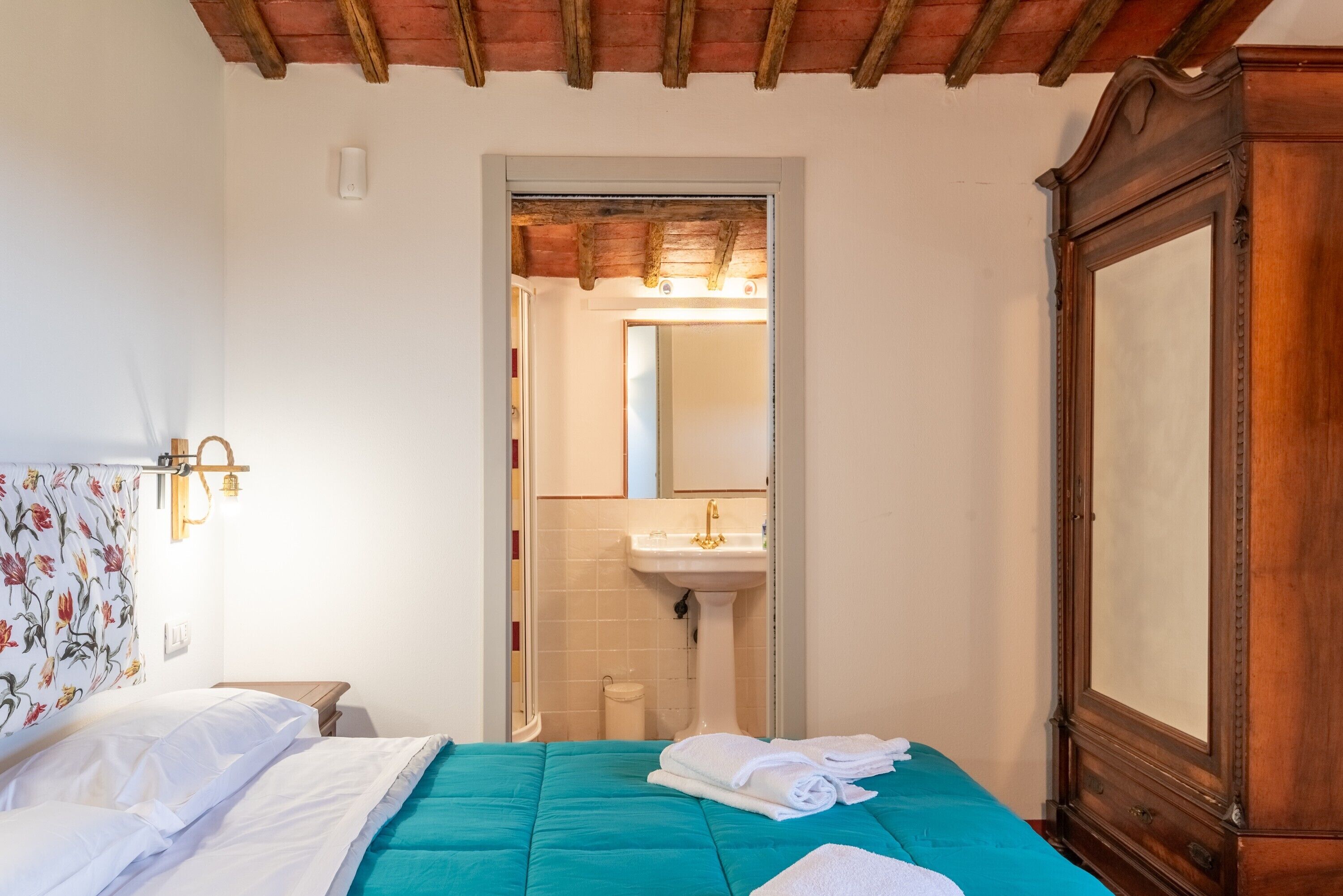 A bedroom with a bed, a wooden wardrobe, a bathroom with a sink, and a mirror.