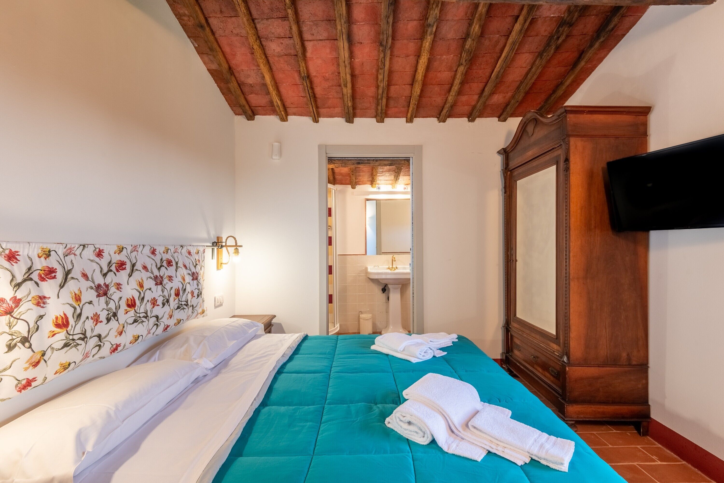 Habitación de hotel con cama, armario de madera, televisor y baño visible a través de una puerta abierta.