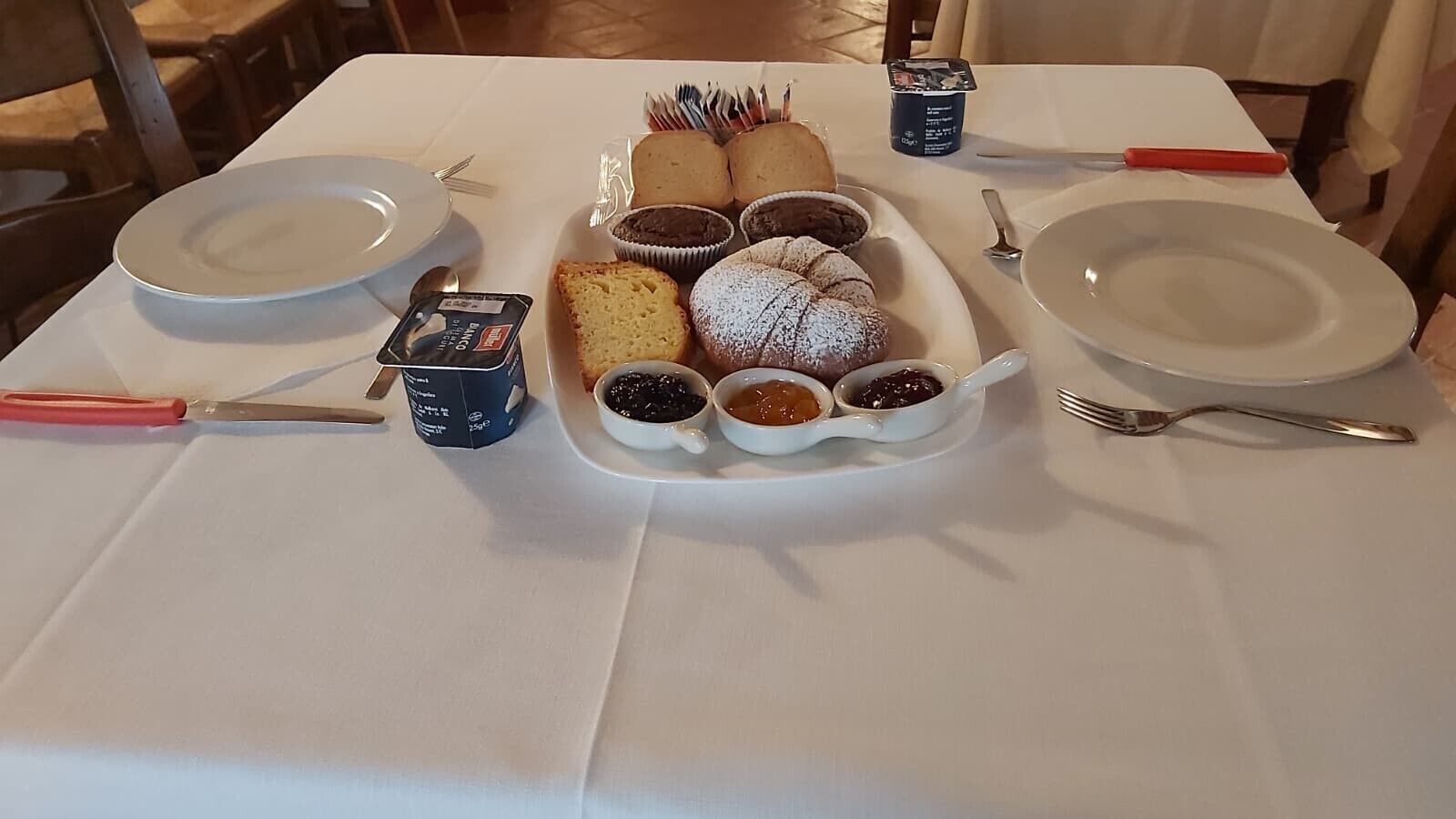 Una mesa dispuesta con una variedad de pasteles, incluyendo muffins y un postre, junto con pequeños recipientes de mermelada.