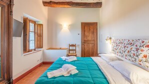 Ein Schlafzimmer mit Bett, Stuhl, Holztür, Wandfernseher und Fenster.