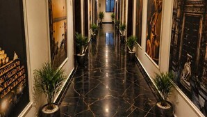 A corridor with a polished black marble floor, flanked by framed artworks and potted plants, leading to a window at the end. - Laxmi Vilas (Varanasi)