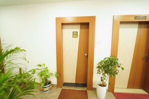 A hallway with two wooden doors, one labeled 'Office' and the other with a wheelchair accessibility sign. There are potted plants on either side of the doors. - Laxmi Vilas (Varanasi)