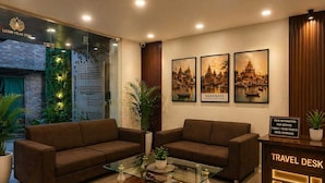 A hotel lobby with two sofas, a glass coffee table, a travel desk, and framed pictures of Varanasi. - Laxmi Vilas (Varanasi)