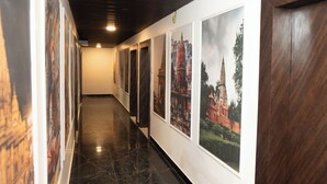 A hallway with framed pictures on the walls, a polished floor, and a wooden door. - Laxmi Vilas (Varanasi)