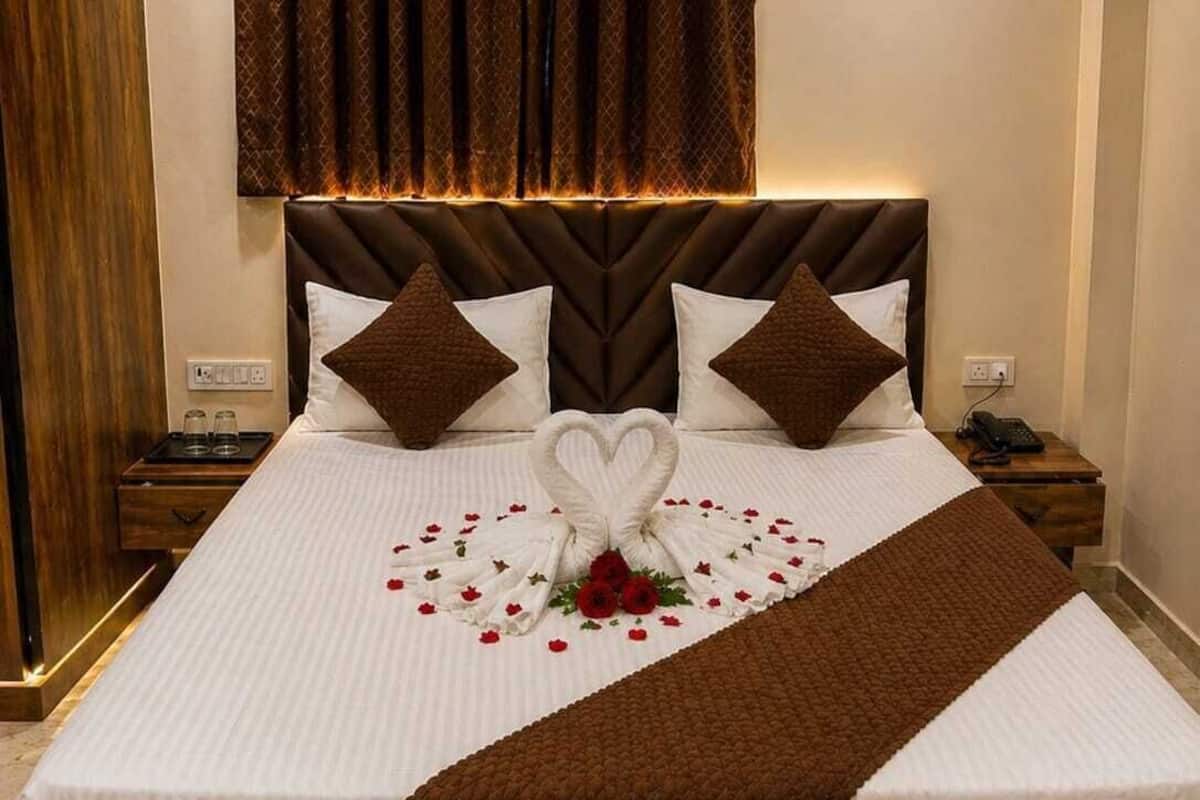 Een net opgemaakt bed met een handdoek in de vorm van een hart, een houten hoofdbord en een nachtkastje met een telefoon.