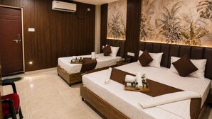 A hotel room with two beds, a ceiling fan, an air conditioning unit, and a mural on the wall. - Laxmi Vilas (Varanasi)
