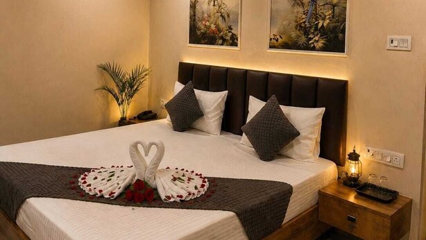 A bedroom with a large bed, a headboard, two wall-mounted paintings, a bedside table with a lamp, and a nightstand. - Laxmi Vilas (Varanasi)