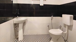 A bathroom with a white sink, toilet, and towel rack. The floor has a black and white geometric pattern. - Laxmi Vilas (Varanasi)
