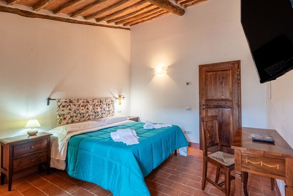 Une chambre à coucher comprenant un lit, une table de chevet, un bureau en bois, une chaise, une armoire en bois et un téléviseur fixé au mur.