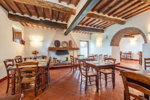 Un'area pranzo con tavoli e sedie in legno, un camino in mattoni e travi a vista sul soffitto.