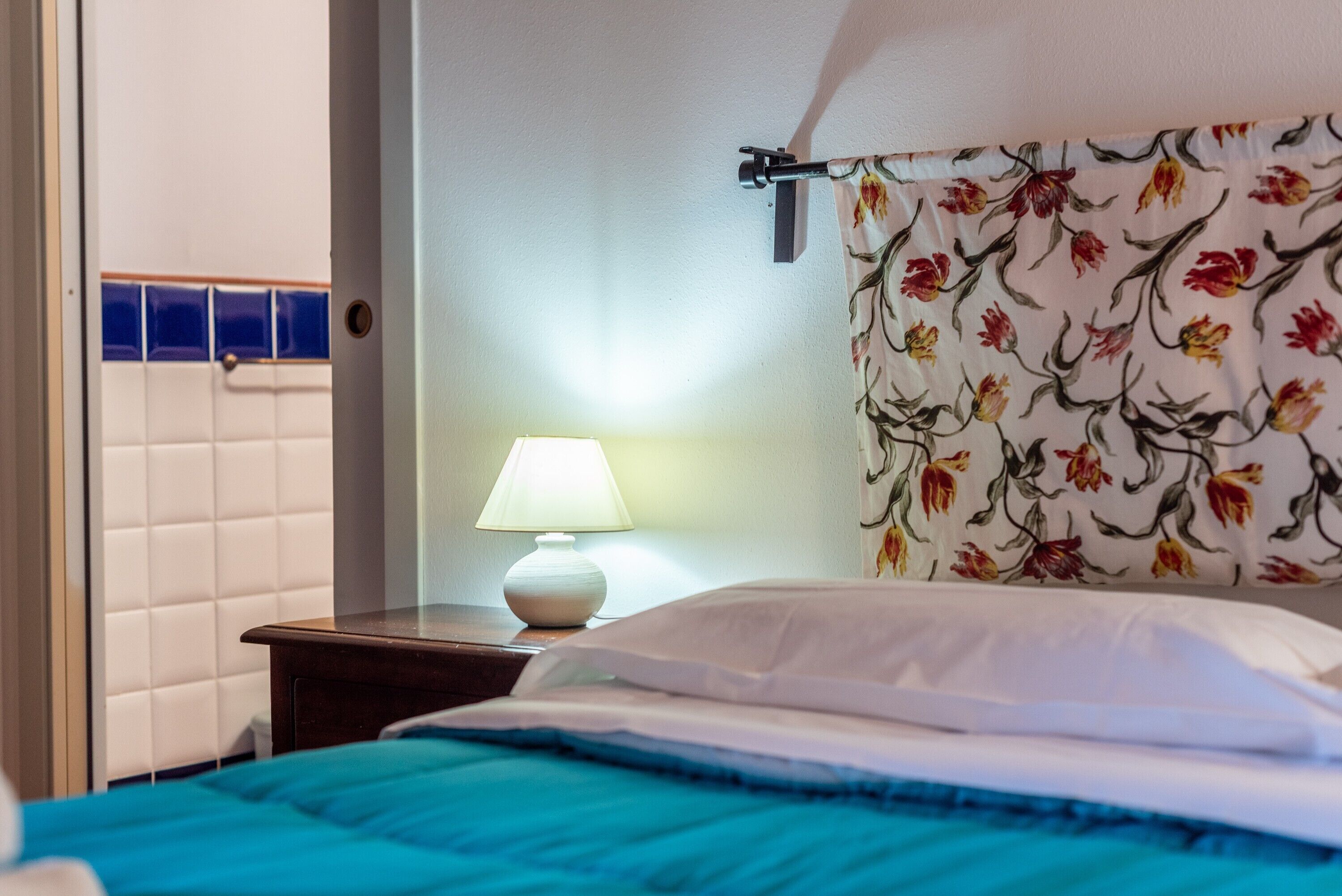 Una habitación de hotel con una cama, una mesita de noche, una lámpara y un cabecero estampado con motivos florales.