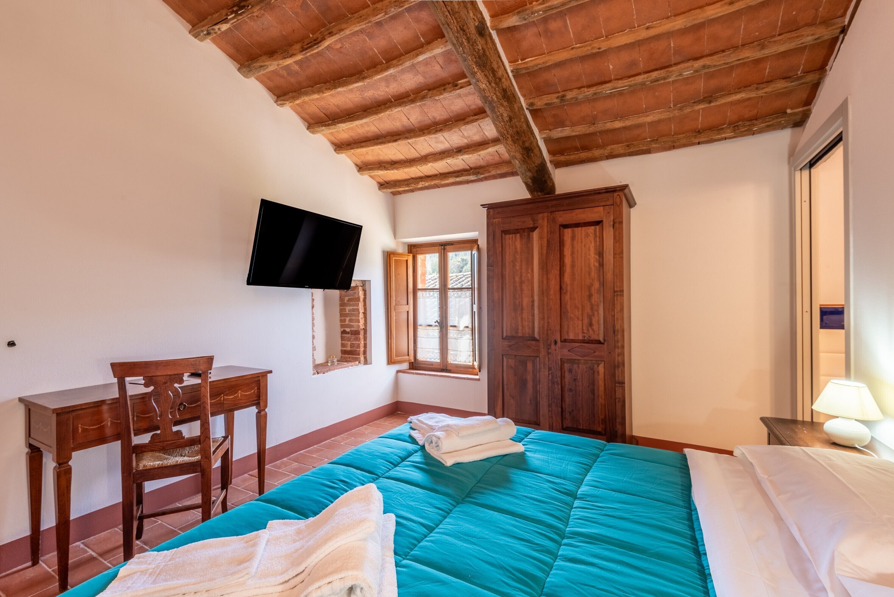 Un dormitorio con una cama, un escritorio, una silla, un televisor y un armario.