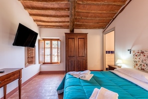 Una camera da letto con soffitto in legno, un letto con biancheria da letto verde acqua, una TV a parete, una finestra e una porta.