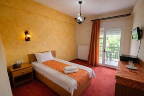 A hotel room with a single bed, a nightstand, a desk with a chair, a TV, and a window with curtains.