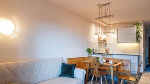 Una sala moderna con un sofá blanco, una mesa de comedor de madera y una cocina con armarios de madera y una planta colgante.