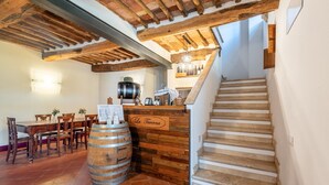 Un interior rústico con vigas de madera a la vista, una barra de madera, una escalera y un comedor con sillas y mesa de madera.