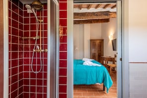 Una stanza con doccia in piastrelle rosse, un letto con copriletto verde acqua, un armadio in legno e un tavolo con una sedia.