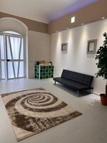 A spacious living area with a large circular rug, a dark sofa, a green cabinet, and a potted plant.