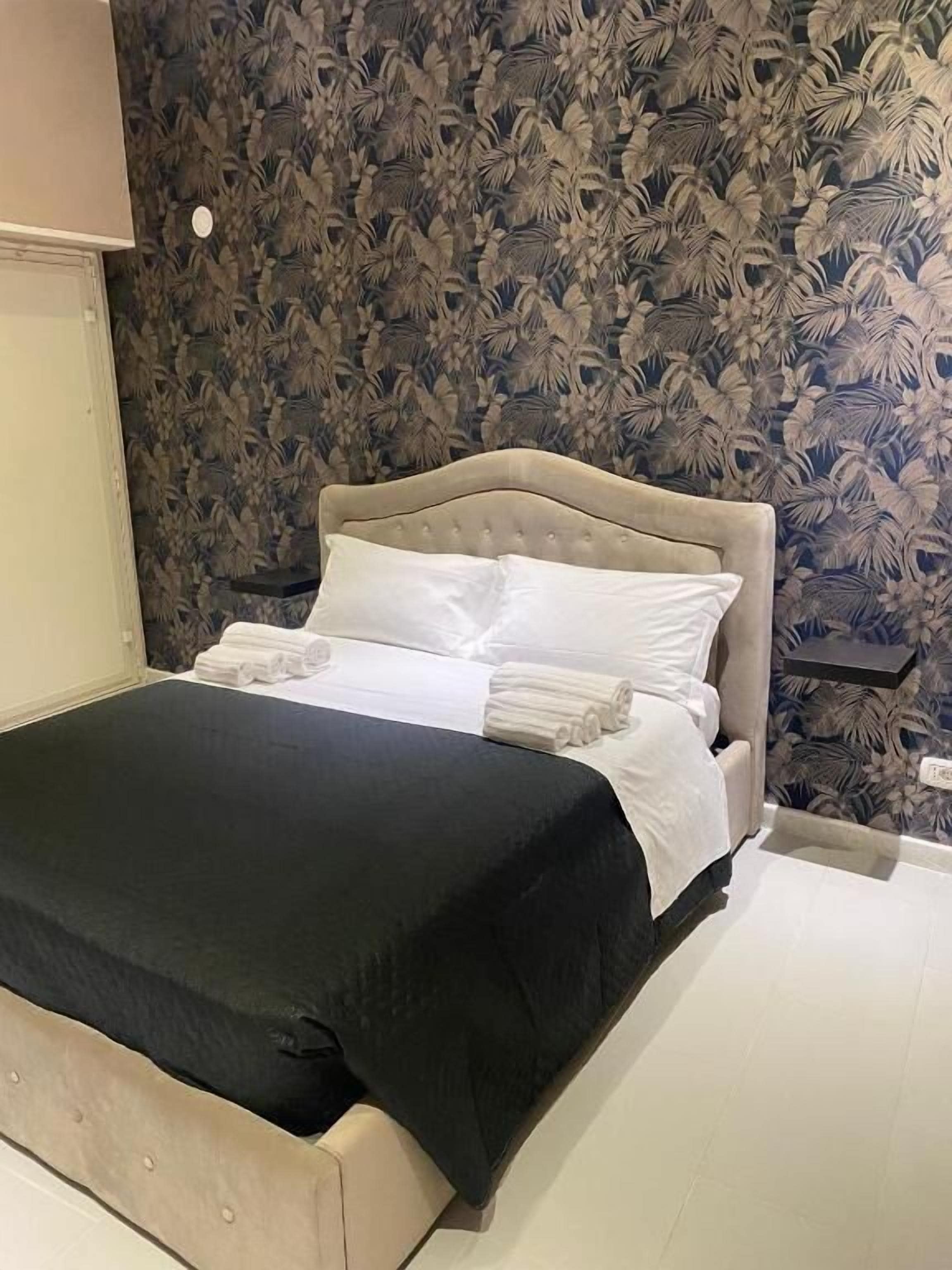 A neatly made bed with a black bedspread and white pillows, a wooden headboard, and a floral wallpaper pattern.