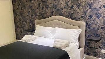 A neatly made bed with a black bedspread and white pillows, a wooden headboard, and a floral wallpaper pattern.