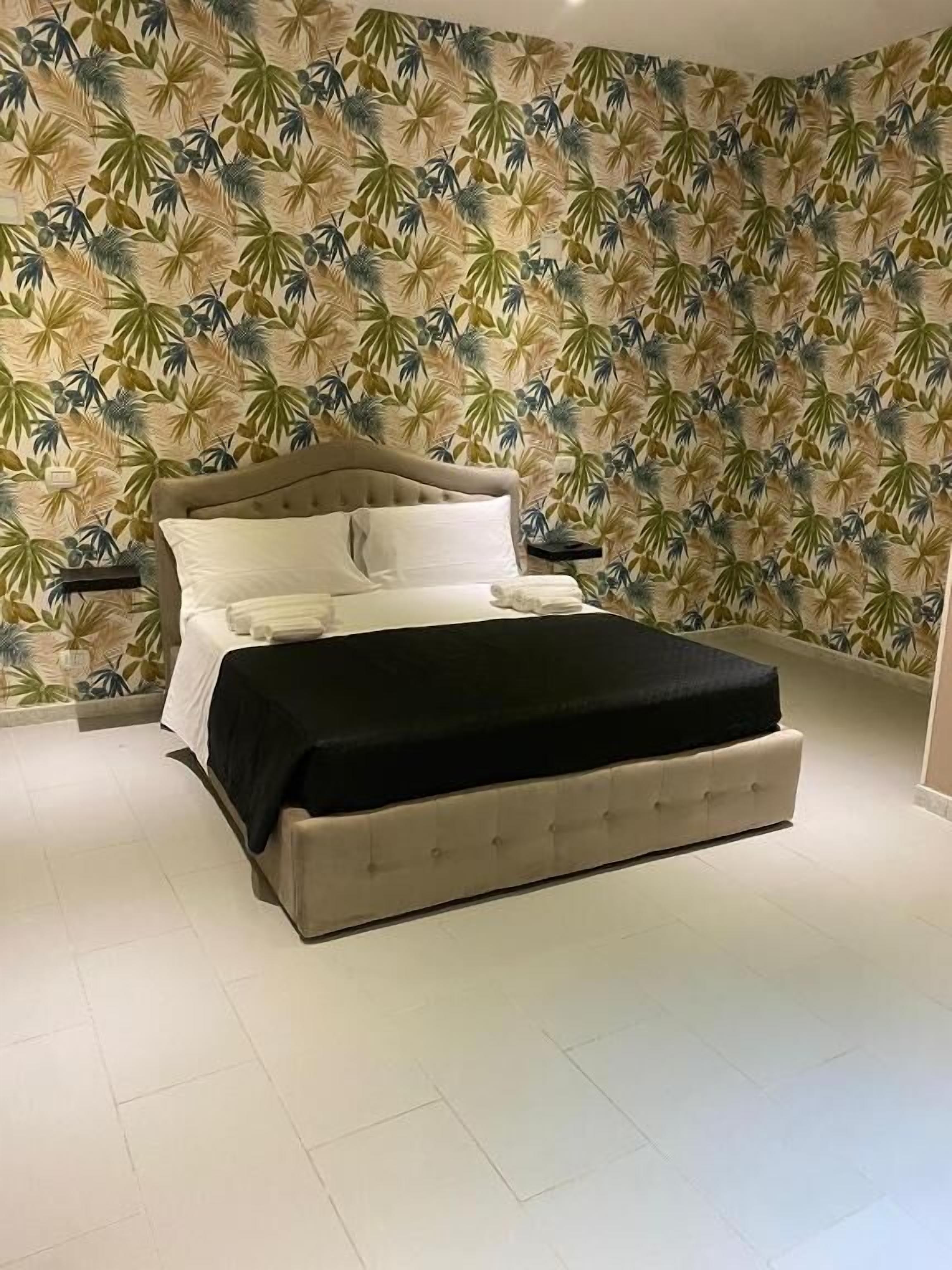 Ein Schlafzimmer mit einem Bett, einem Nachttisch und einer Wand mit tropischem Blattmuster.