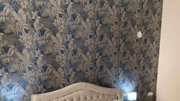 A neatly made bed with a dark quilt, white pillows, and a beige headboard. There are two bedside lamps on either side of the bed. - Melody rooms (Syracuse)