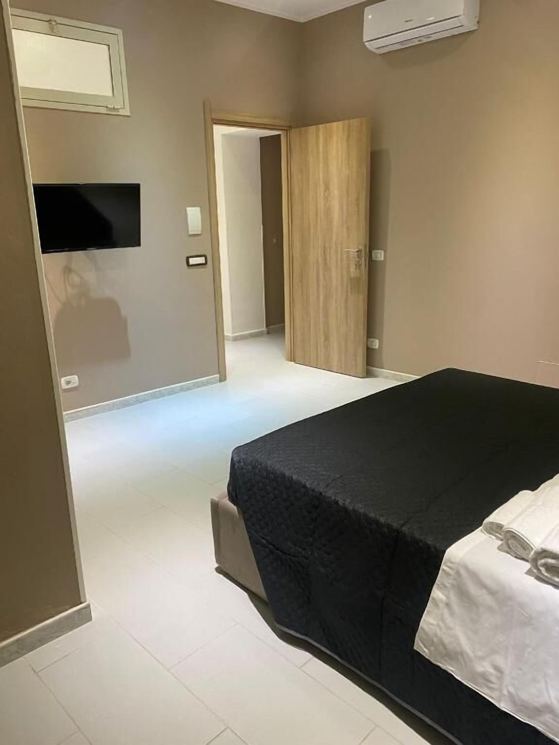 Una camera d'albergo con un letto, una televisione e una porta che dà su un'altra stanza.