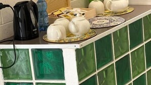A kitchen counter with a green and white tiled backsplash, a black coffee maker, white teapots, and a wooden box. - Melody rooms (Syracuse)