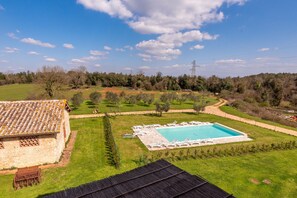 Una piscina con sillas de descanso, un edificio de piedra y un área verde con árboles.