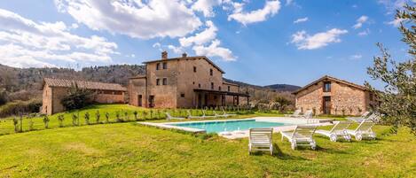 A large stone building with a swimming pool and lounge chairs.