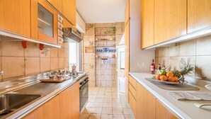 A narrow kitchen with wooden cabinets, a stainless steel sink, and a countertop with fruits and a bottle. - Desire for the Sea (Gallipoli)
