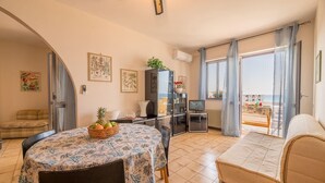 A cozy room with a bed, a dining table with a fruit basket, a TV, and a view of the beach. - Desire for the Sea (Gallipoli)