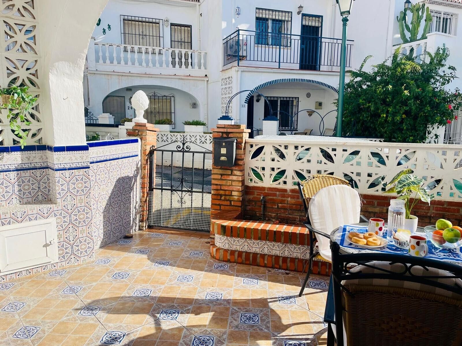 Un patio con piso de baldosas, una silla de mimbre y una mesa con comida y bebidas.