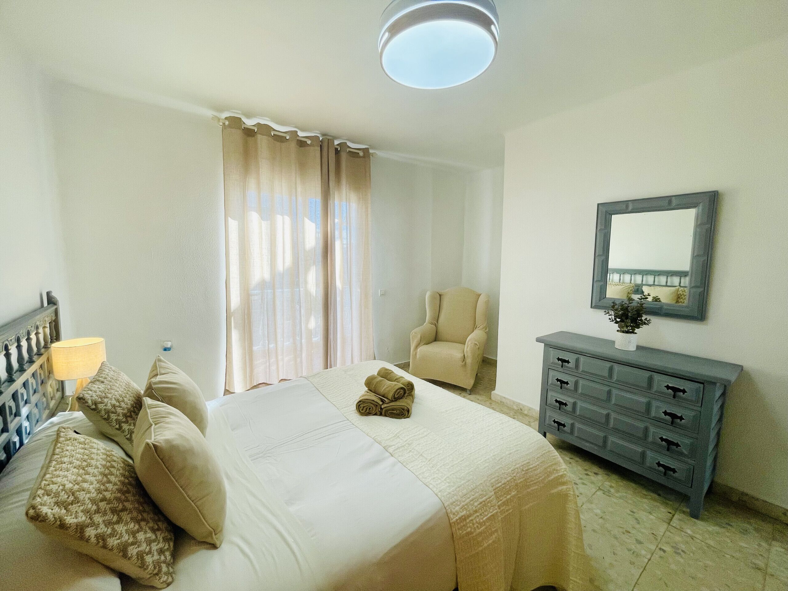 A hotel room with a bed, a chair, a dresser, and a window with curtains.