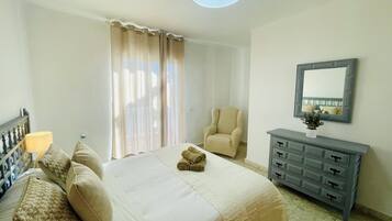 A hotel room with a bed, a chair, a dresser, and a window with curtains.