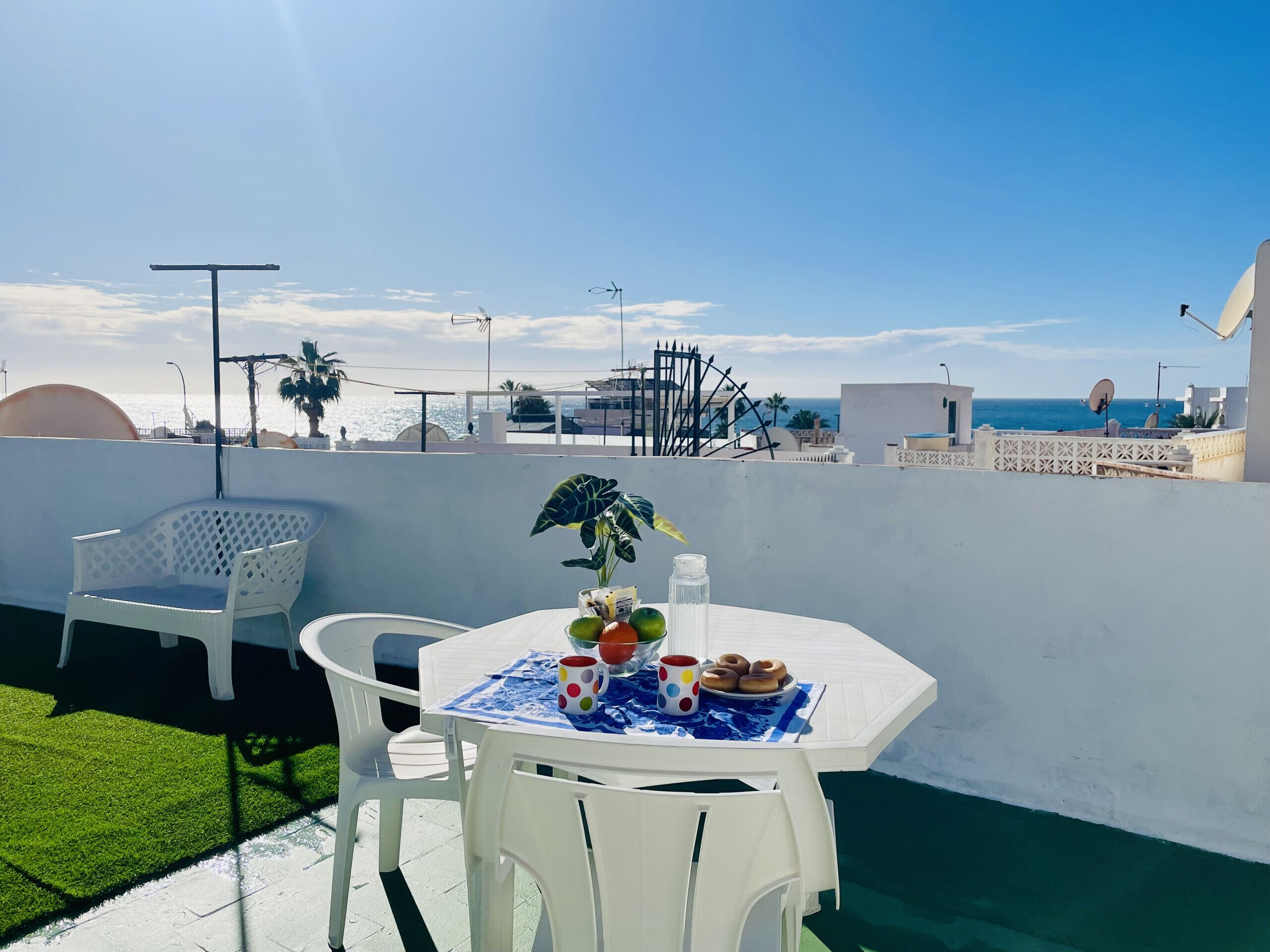 A rooftop terrace with a table set for two, a chair, and a potted plant.
