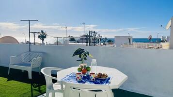 A rooftop terrace with a table set for two, a chair, and a potted plant.