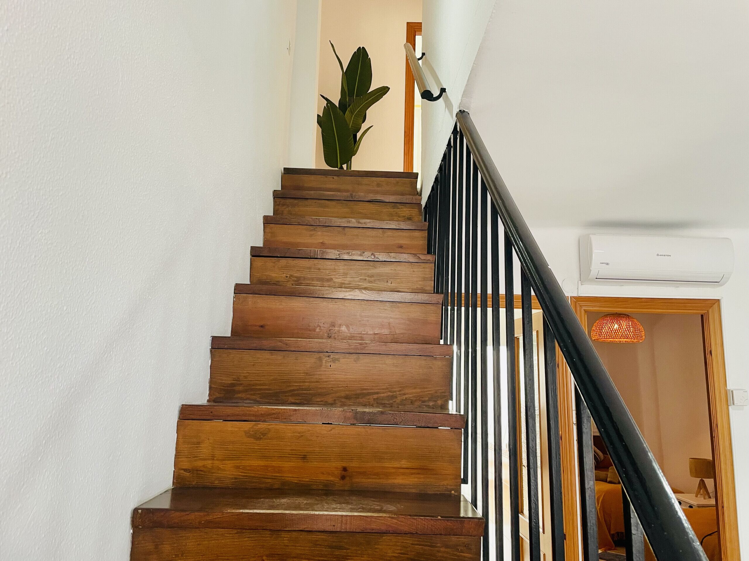 A wooden staircase with black railings, a potted plant, and an air conditioning unit on the wall.