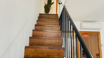 A wooden staircase with black railings, a potted plant, and an air conditioning unit on the wall.