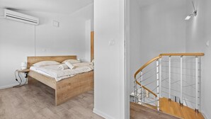 A bedroom with a wooden bed, a nightstand, an air conditioner, and a staircase with a wooden railing. - Apartment Susanne 2 with Shared Pool near Porec (Kukci)