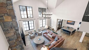 Amplia sala de estar con una pared de acento de piedra, ventanas grandes, chimenea y zona de comedor con televisor.