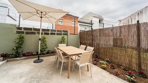 Un patio con una mesa, sillas, un paraguas grande y una valla de bambú.