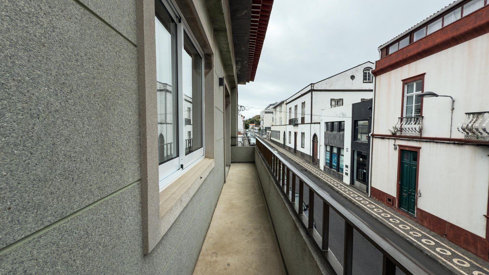 A narrow corridor with a concrete floor, bordered by buildings with large windows and balconies.
