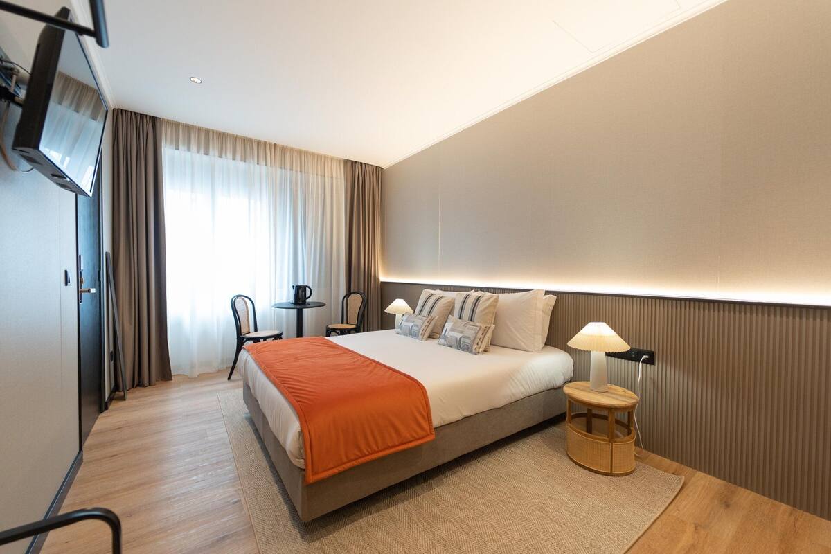 Hotellihuone, jossa on sänky, yöpöytä, lamppu ja näkymä ulos.