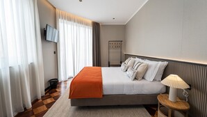 Une chambre d’hôtel moderne dotée d’un grand lit, d’un téléviseur à écran plat, d’une table de chevet avec une lampe et offrant une vue sur la ville grâce à de grandes fenêtres.