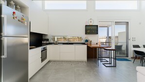 A modern kitchen with white cabinetry, a stainless steel refrigerator, a built-in oven, a dining area with a table and chairs, and a view through a glass door. - Villa Ginevra: Exclusive Luxury and Wellbeing Near Otranto (Otranto)